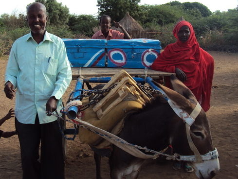Man standing beside donkey pulling cart with school supplies
